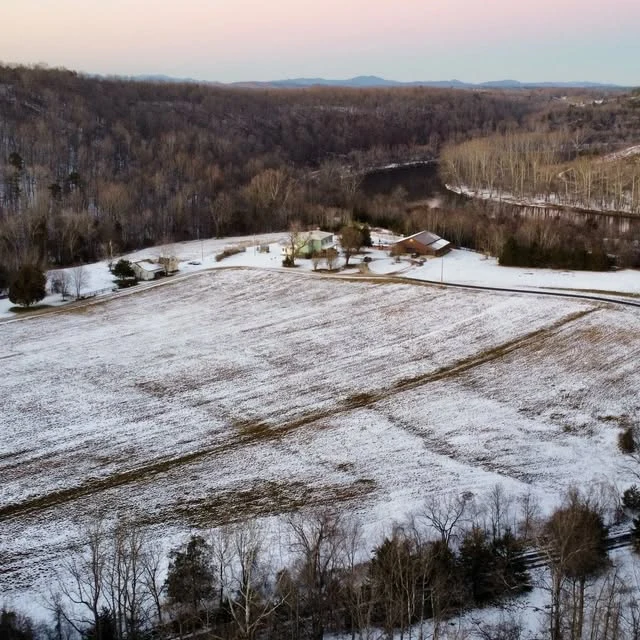 An aerial view of the property dusted with snow beside the wooded river